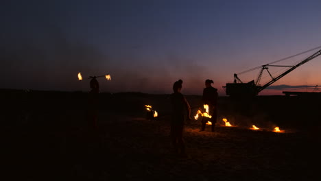 Fire-show-three-women-in-their-hands-twist-burning-spears-and-fans-in-the-sand-with-a-man-with-two-flamethrowers-in-slow-motion